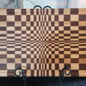 Wooden cutting board stained in a checkerboard pattern with squares of varying sizes, creating an op…