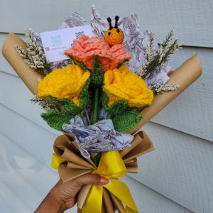 Photograph of a bouquet of crocheted flowers with a crocheted bumblebee on top. 